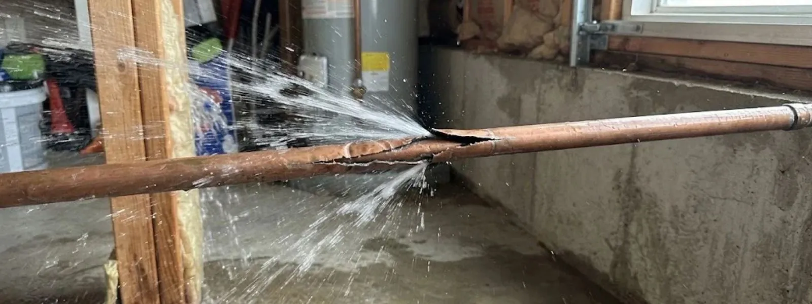 Burst copper pipe spraying water in a basement along a concrete wall