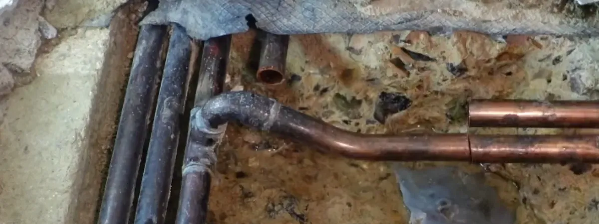 Opened concrete slab exposing corroded and copper pipes where a slab leak is being repaired